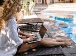 Woman Working By Accommodation Pool As Digital Nomad