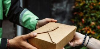 Person in green and black jacket delivering takeout food to woman who didn't have energy to cook
