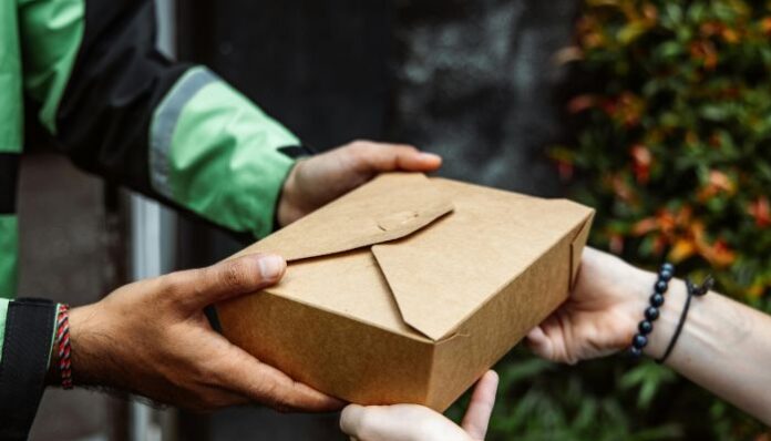 Restaurant to go Packaging Person in green and black jacket delivering takeout food to woman who didn't have energy to cook