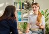 Young Woman With Long Blonde Hair and White T Shirt Discussing Mental Health With Brunette Professional, Likely a Therapist or Psychologist