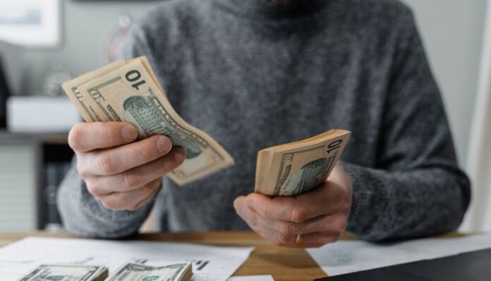 Young male medical student counting cash and determining his budget using calcuator and other tools