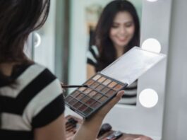 Which Colour Palette Eyeshadow Fits Your Eye Color? Woman putting on eyeshadow in mirror using eye shadow palette