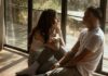 How To Talk About Kinks With Your Partner Couple sitting near a window in their home, talking about their personal bedroom kinks