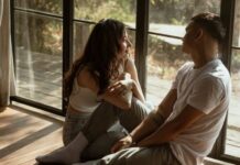 How To Talk About Kinks With Your Partner? Couple sitting near a window in their home, talking about their personal bedroom kinks