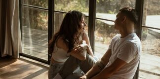 How To Talk About Kinks With Your Partner Couple sitting near a window in their home, talking about their personal bedroom kinks