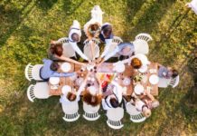 How to Plan a Memorable Home Wedding Without Overspending Wedding Party gathered around a wooden table at a backyard wedding reception, celebrating with a toast.