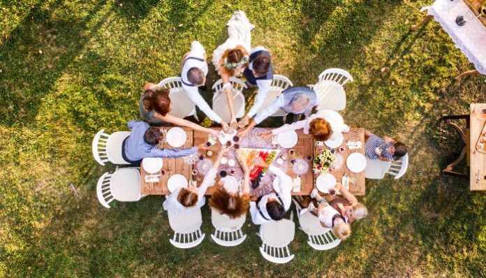 memorable home wedding Wedding Party gathered around a wooden table at a backyard wedding reception, celebrating with a toast.